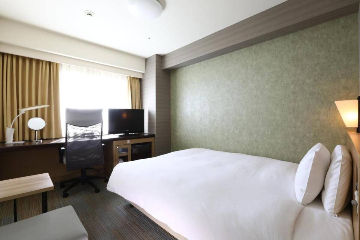 Ein Hotelzimmer mit einem großen Bett, einem Schreibtisch mit Stuhl, einem Fernseher und einer Lampe.