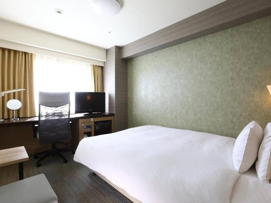 A hotel room with a large bed, a desk with a chair, a television, and a lamp.