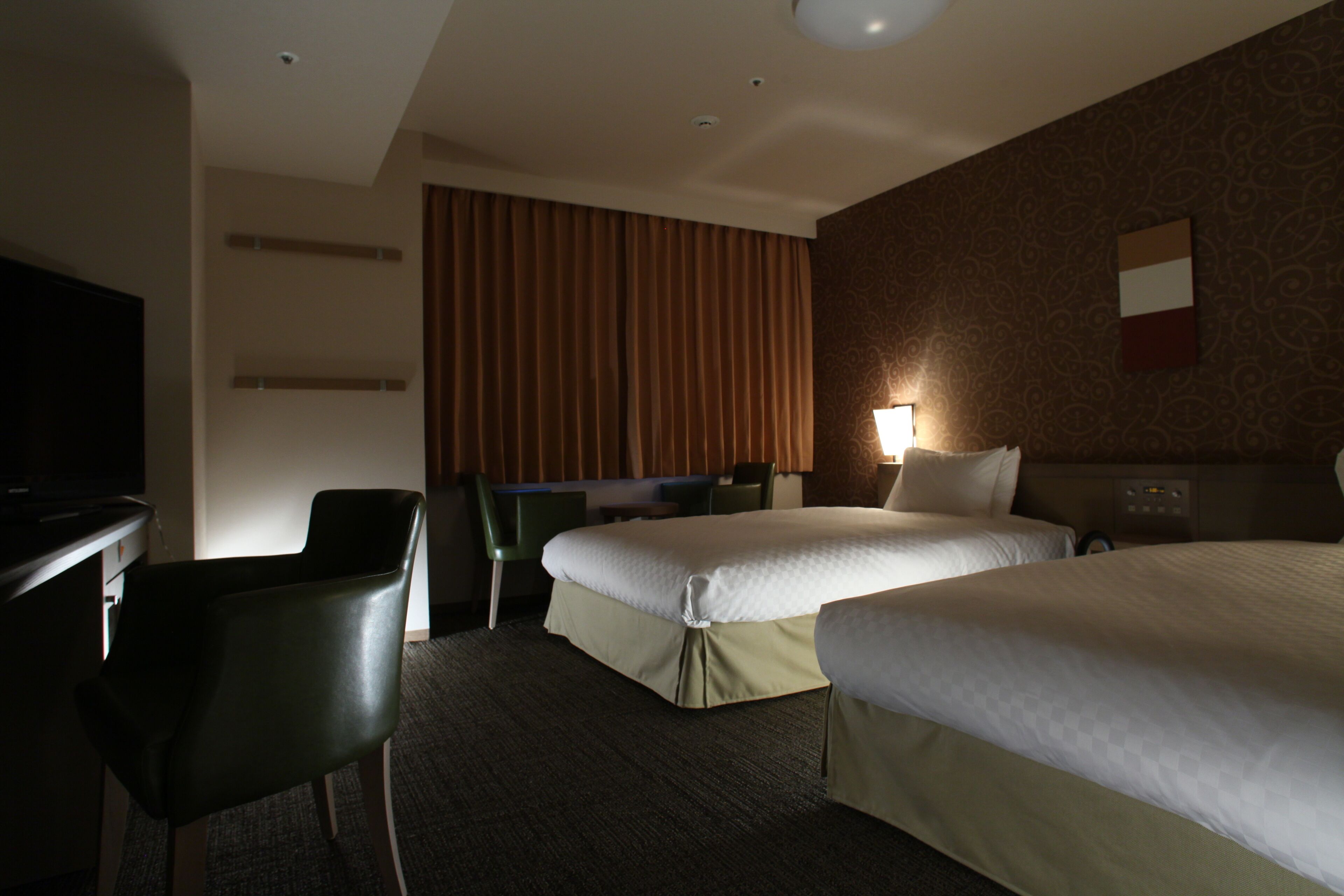 A hotel room with two beds, a desk, a chair, and a television.