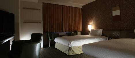 A hotel room with two beds, a desk, a chair, and a television.