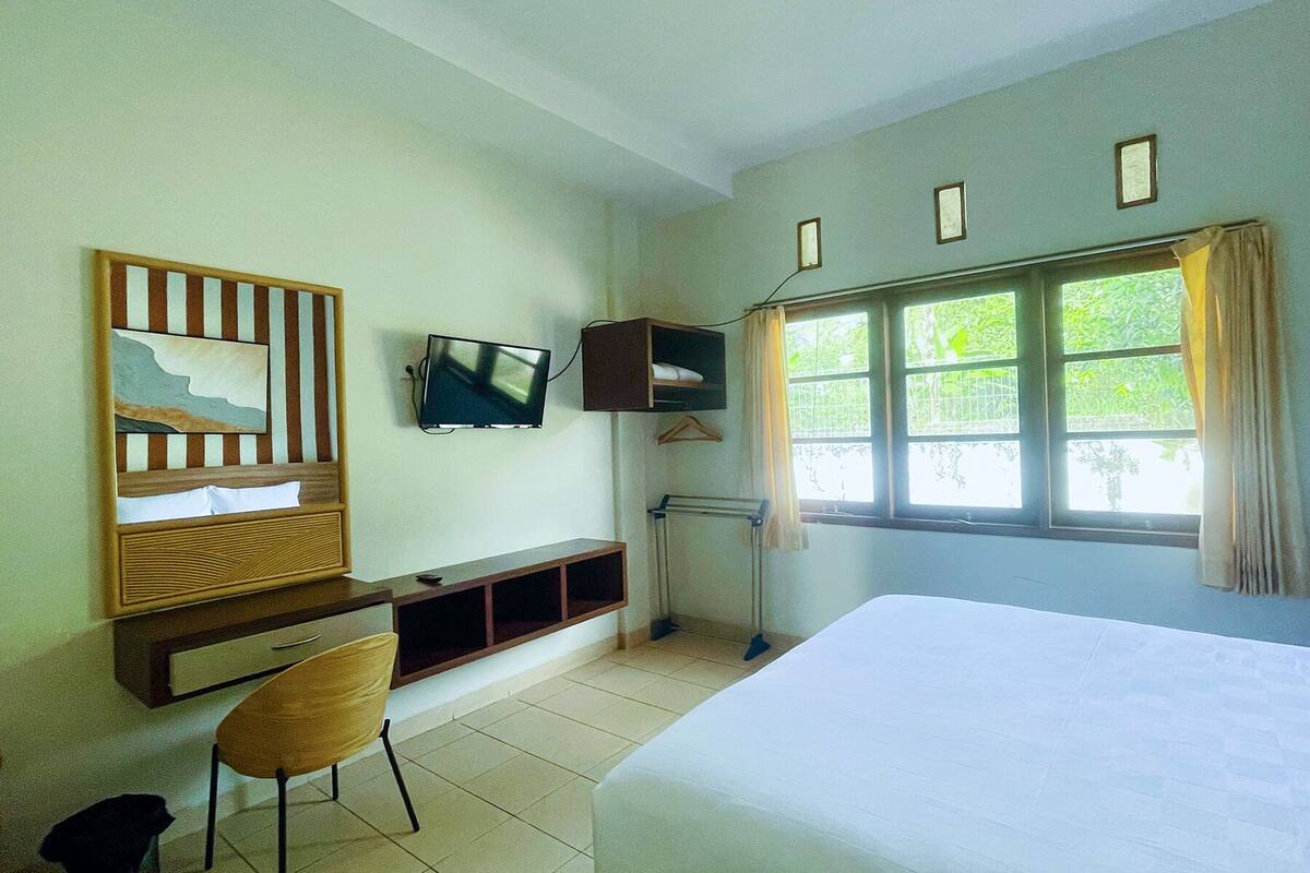 Ein Hotelzimmer mit einem Bett, einem Schreibtisch mit Stuhl, einem an der Wand befestigten Fernseher und einem Fenster mit Vorhängen.
