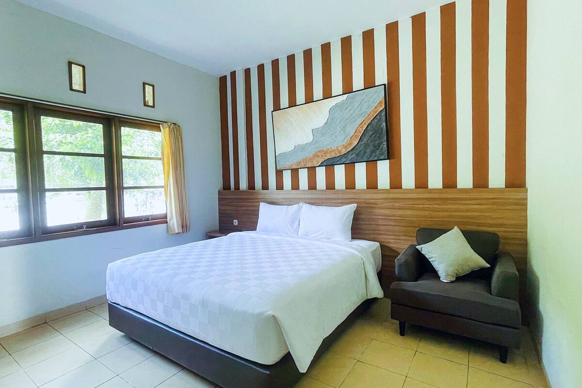 Ein Schlafzimmer mit Bett, Nachttisch, Stuhl, Fenster und Wand mit Streifenmuster und einem Gemälde.