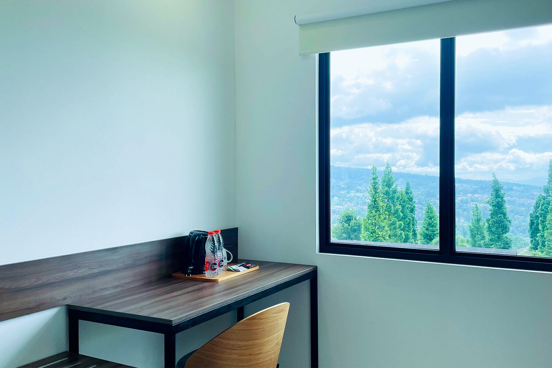 A room with a desk, chair, and a large window with a view of trees and mountains.