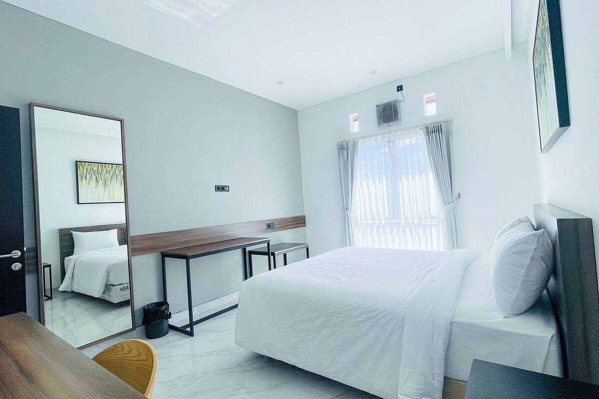 Ein modernes Hotelzimmer mit einem großen Bett, einem Schreibtisch, einem Spiegel und einem Fenster mit Vorhängen.