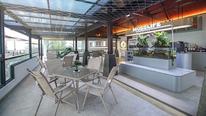 A modern cafe with a glass ceiling, a coffee bar, and a seating area with wicker chairs and a table. - Alfa Jivana Resort  (Cisarua)