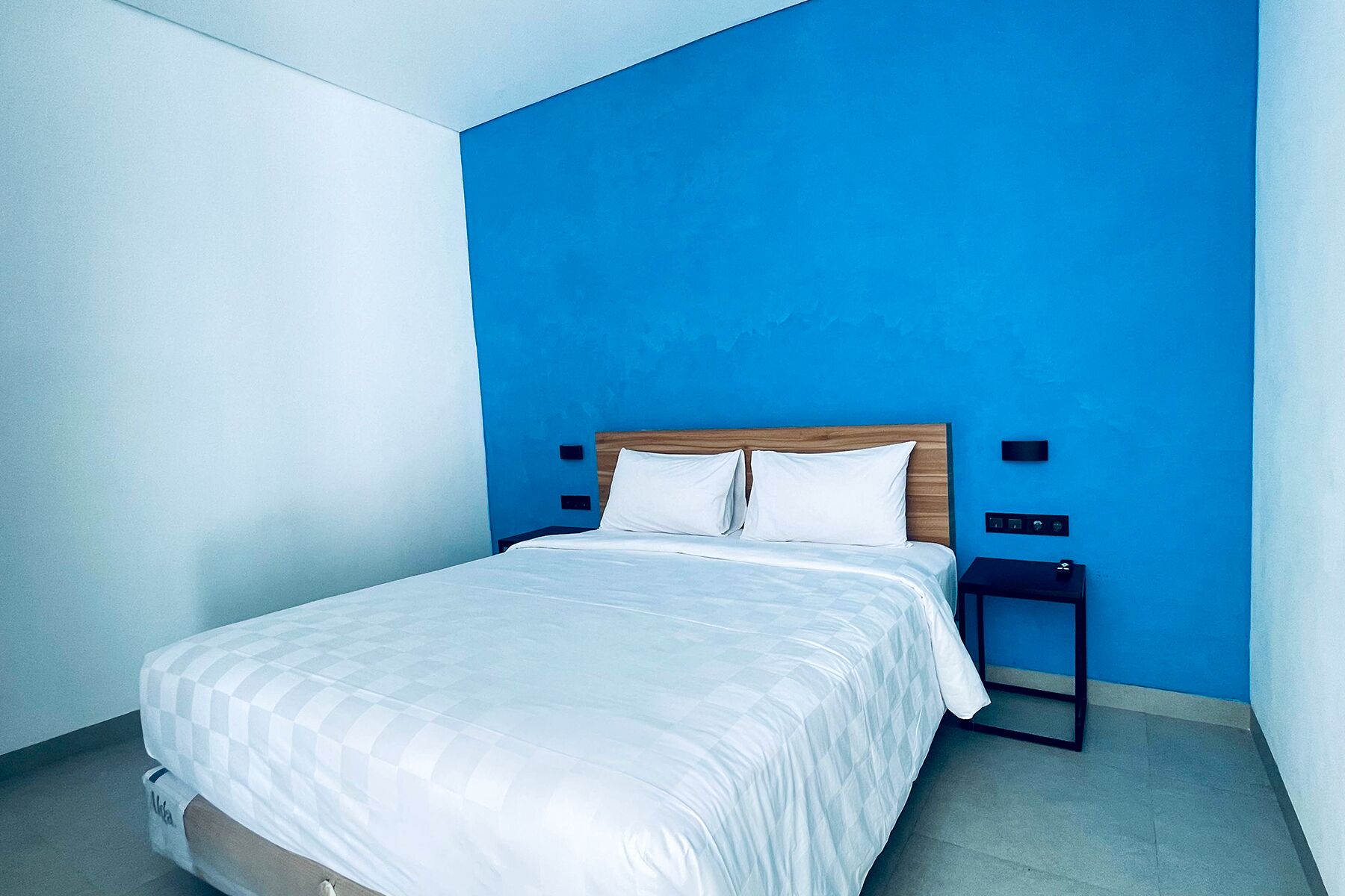 Ett modernt hotellrum med en stor säng, en sänggavel i trä och en blå accentvägg.
