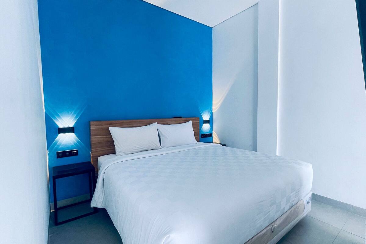 Ein modernes Hotelzimmer mit einem großen Bett, einem Holzkopfteil und zwei an der Wand befestigten Nachttischen.