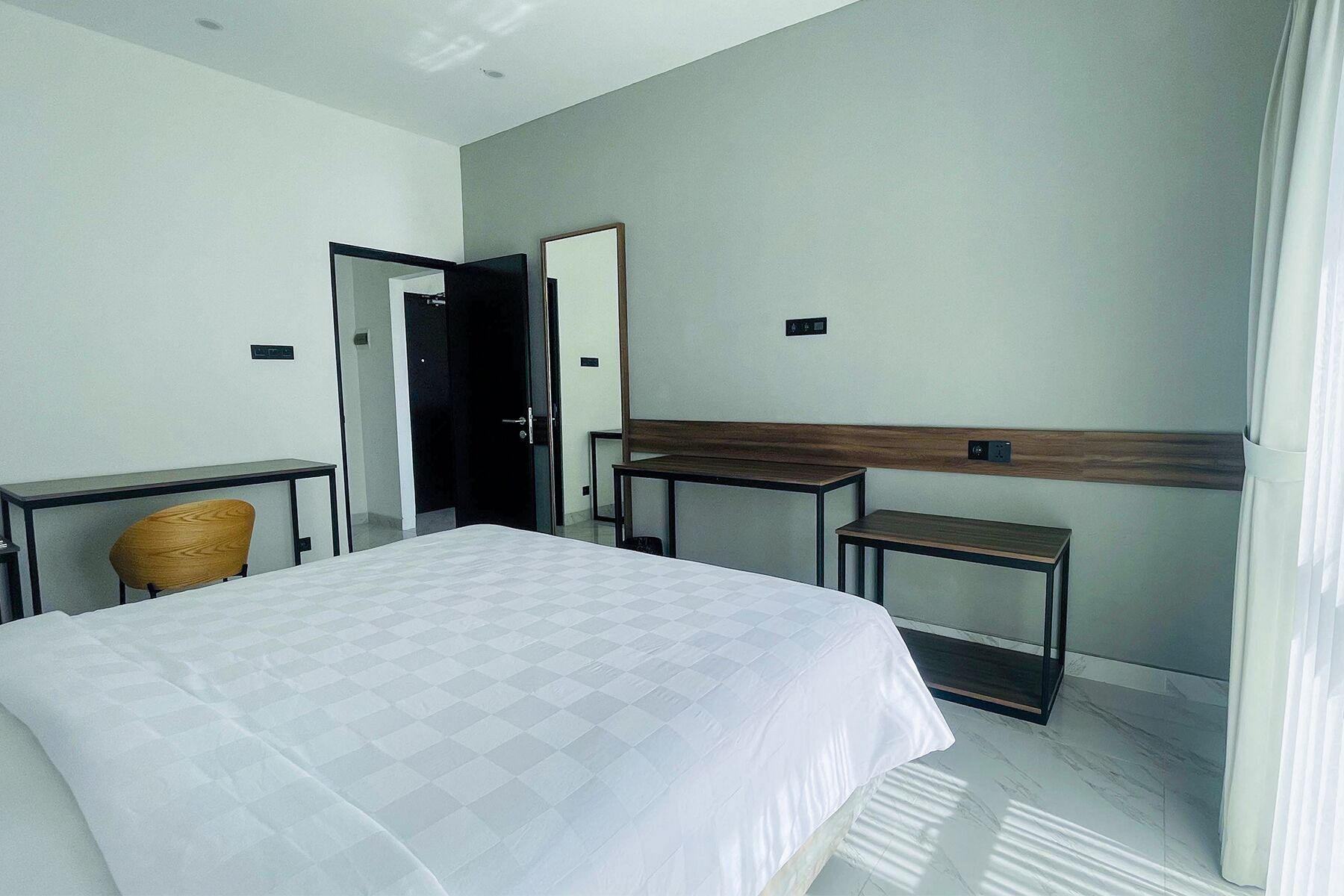 A modern hotel room with a large bed, a desk, a chair, and a mirror.