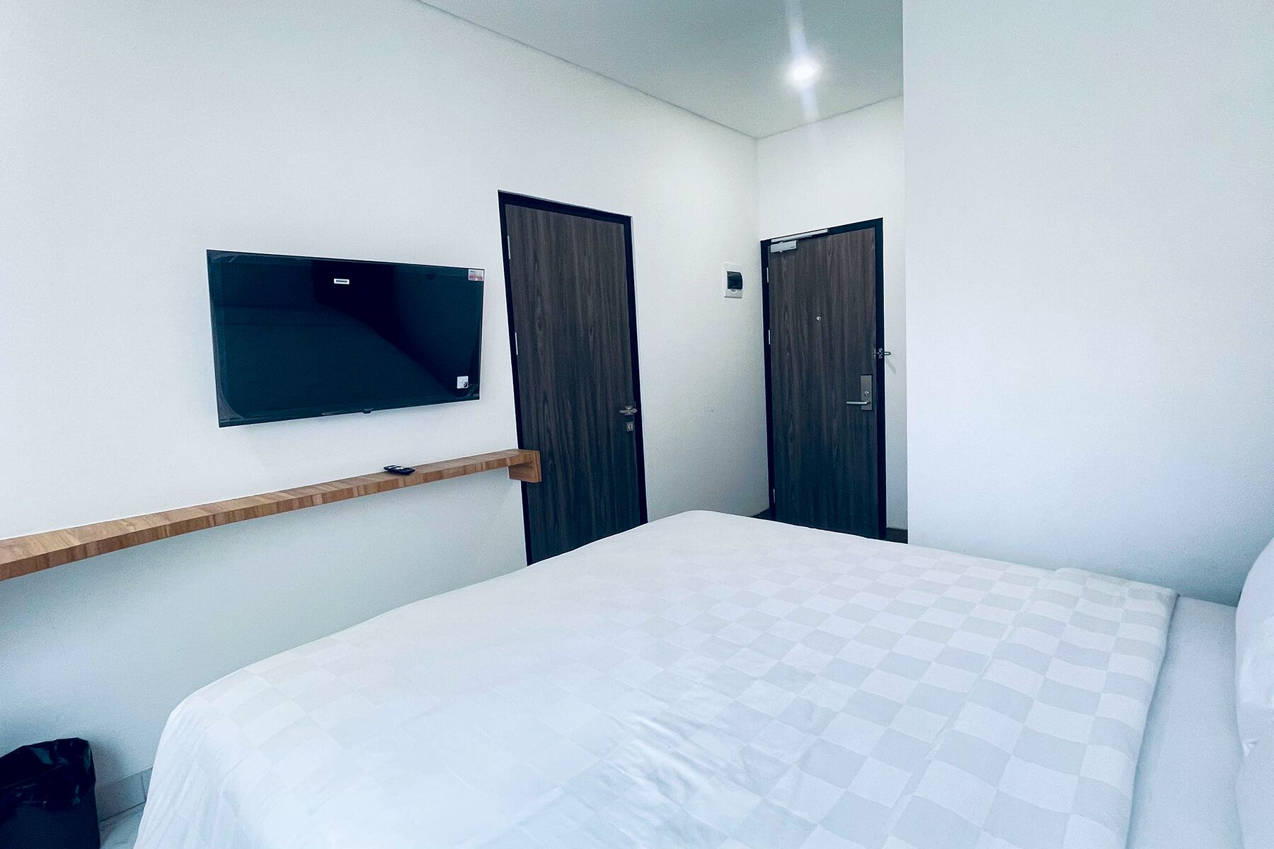 Una camera d'albergo con un letto, una TV a muro e due porte.