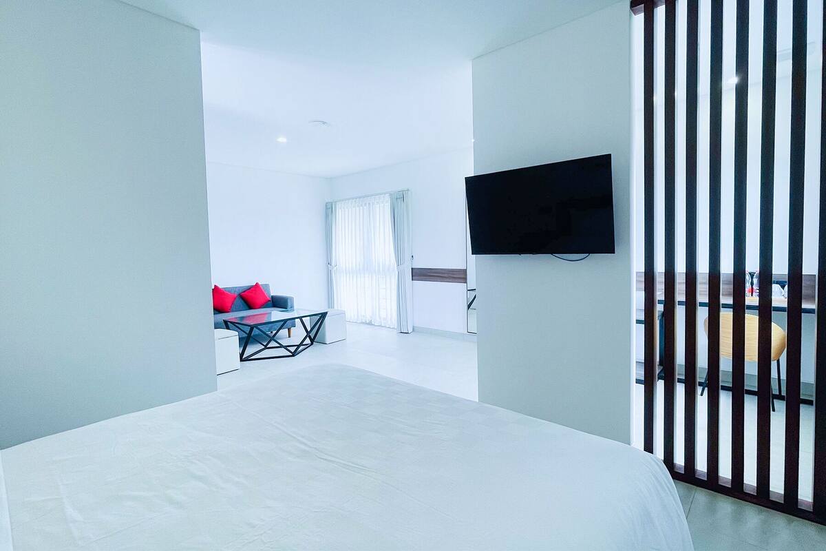 Ein modernes Hotelzimmer mit Bett, einem an der Wand befestigten Fernseher und einem Balkon mit Geländer.