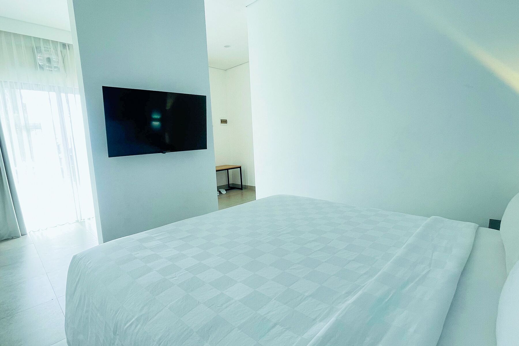 A hotel room with a bed, a television mounted on the wall, and a small table with a chair.