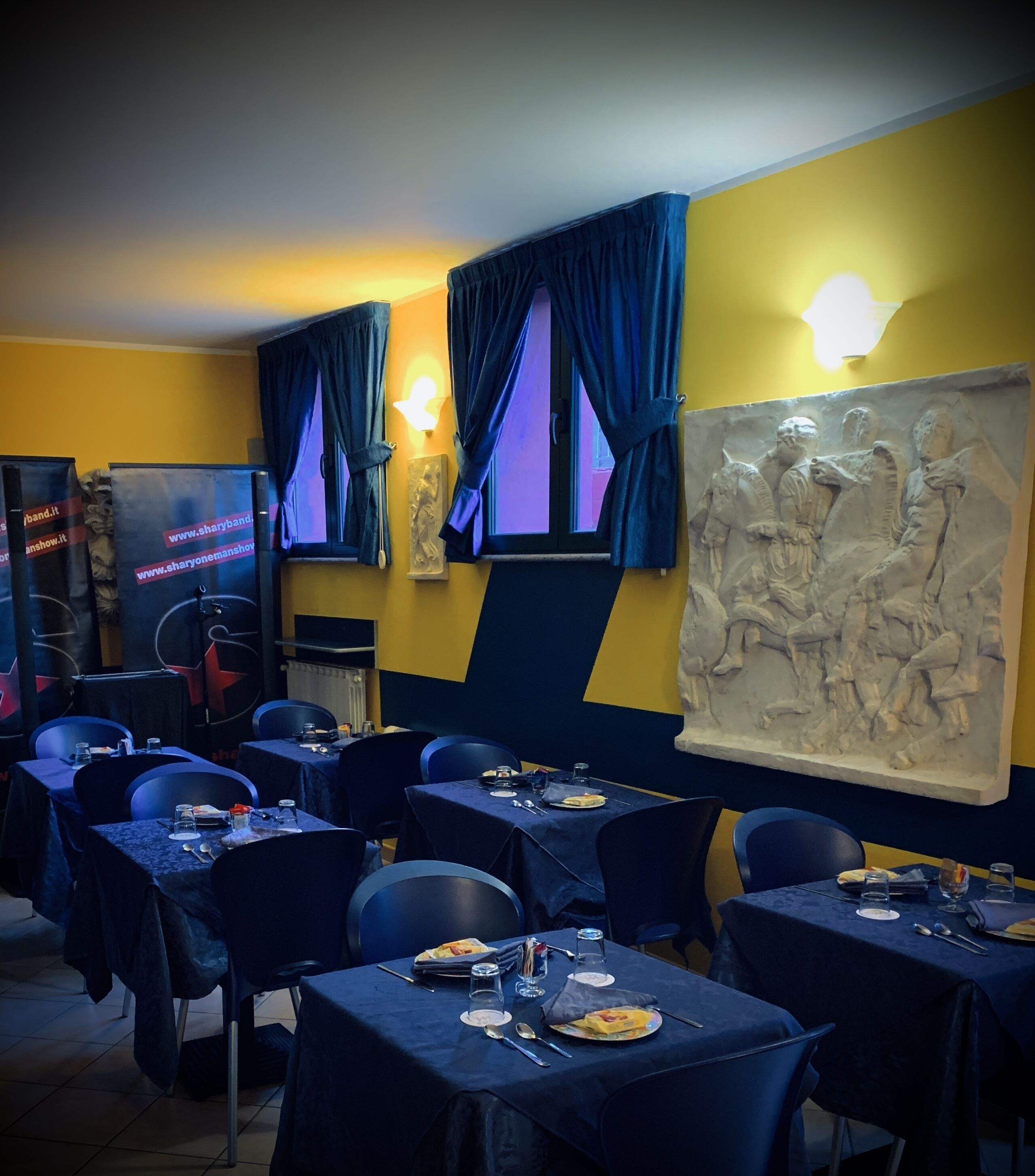Un restaurant avec des tables dressées pour le service, une grande sculpture murale et un panneau lumineux au néon accroché au mur.
