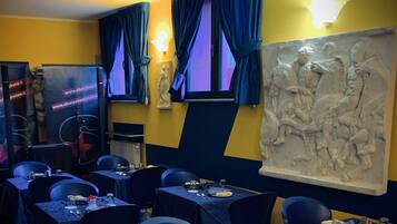Un restaurant avec des tables dressées pour le service, une grande sculpture murale et un panneau lumineux au néon accroché au mur.
