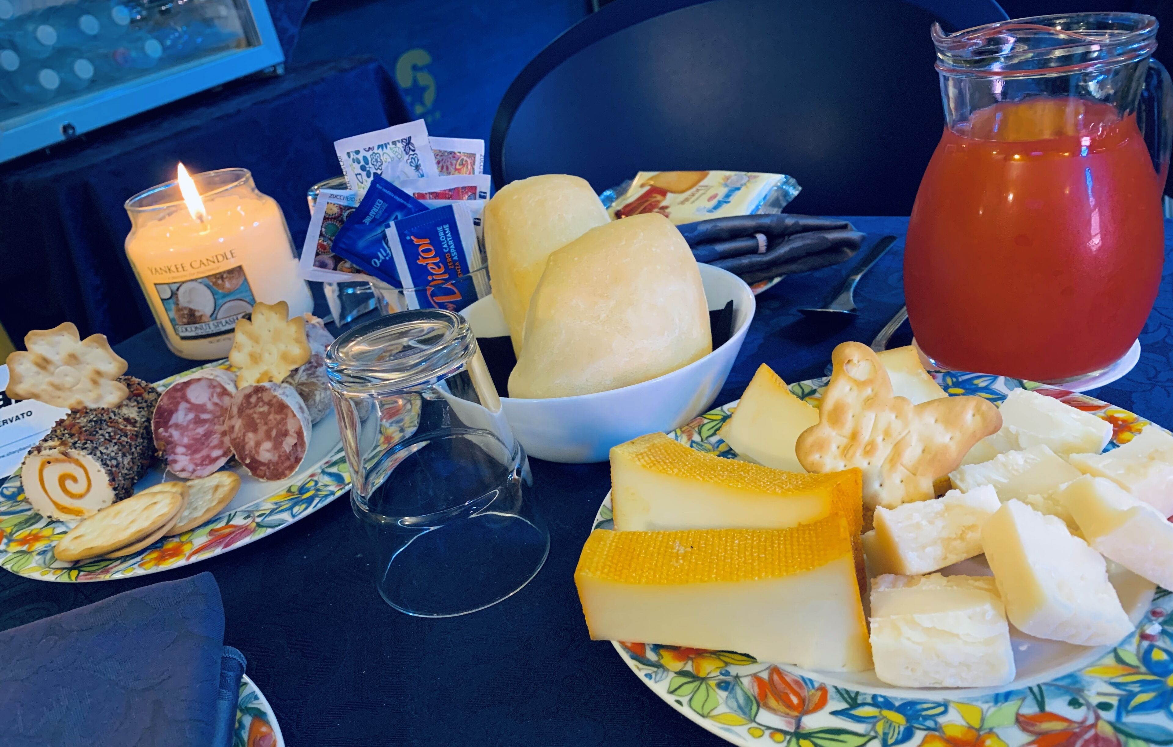 Una mesa con varios quesos, galletas, una vela y una jarra de jugo.