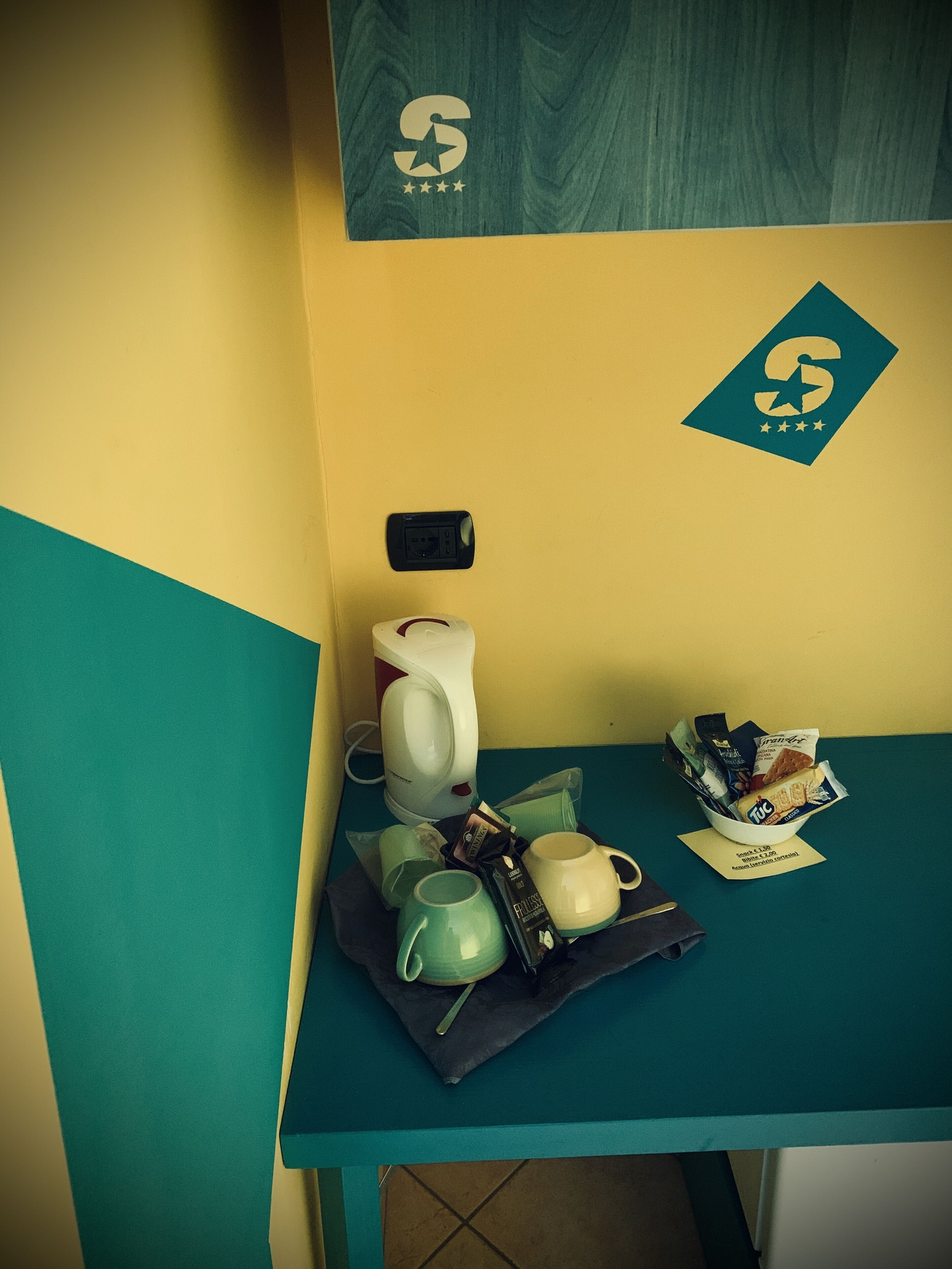 A teal-colored table with a coffee maker, mugs, and snacks.
