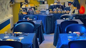 A restaurant with tables set for dining, chairs, and a television screen in the background. - Hotel Residence S (Front)