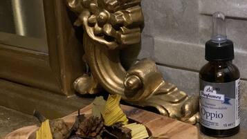 Un bol en bois rempli de fleurs séchées et de pommes de pin, un cadre décoratif doré et un flacon de parfum Oppio.