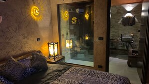 A bedroom with a bed, leopard print bedding, a glass door leading to a bathroom, and a stone wall. - Hotel Residence S (Front)