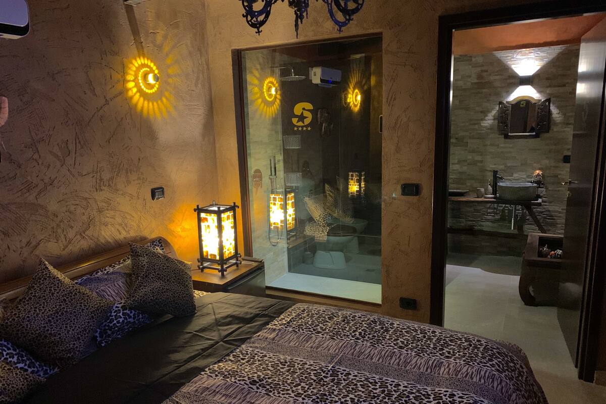 A bedroom with a bed, leopard print bedding, a glass door leading to a bathroom, and a stone wall.