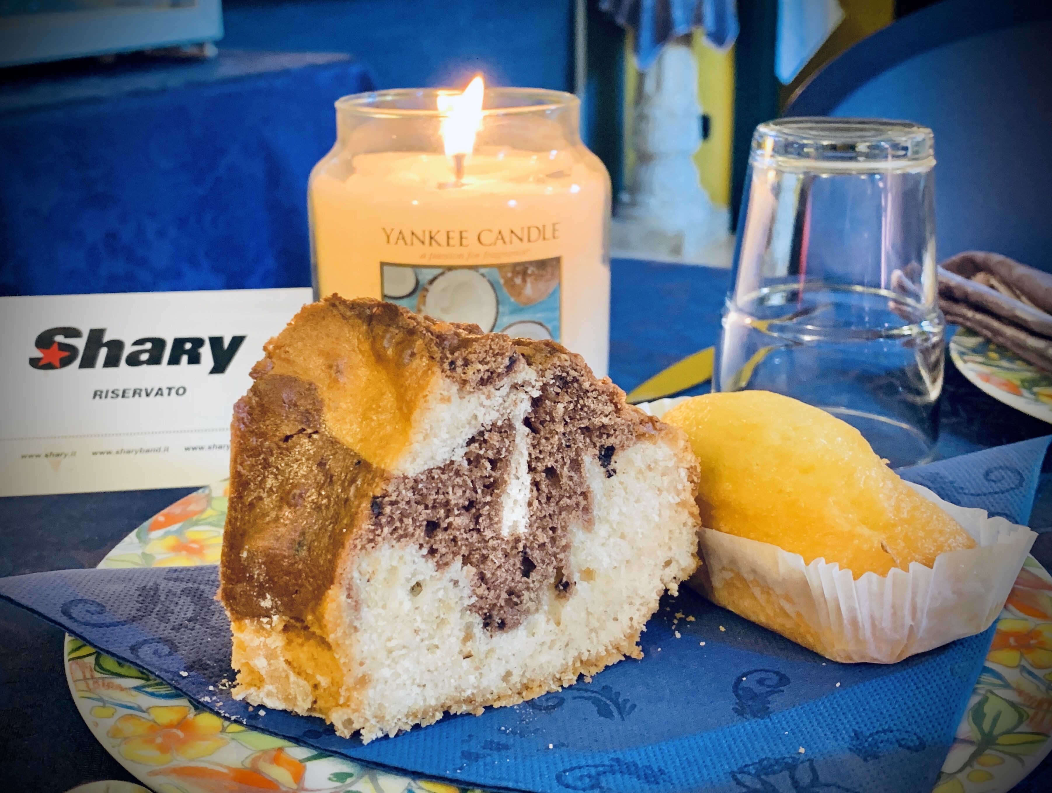 Una porción de pastel con una vela y un vaso de agua sobre una mesa.