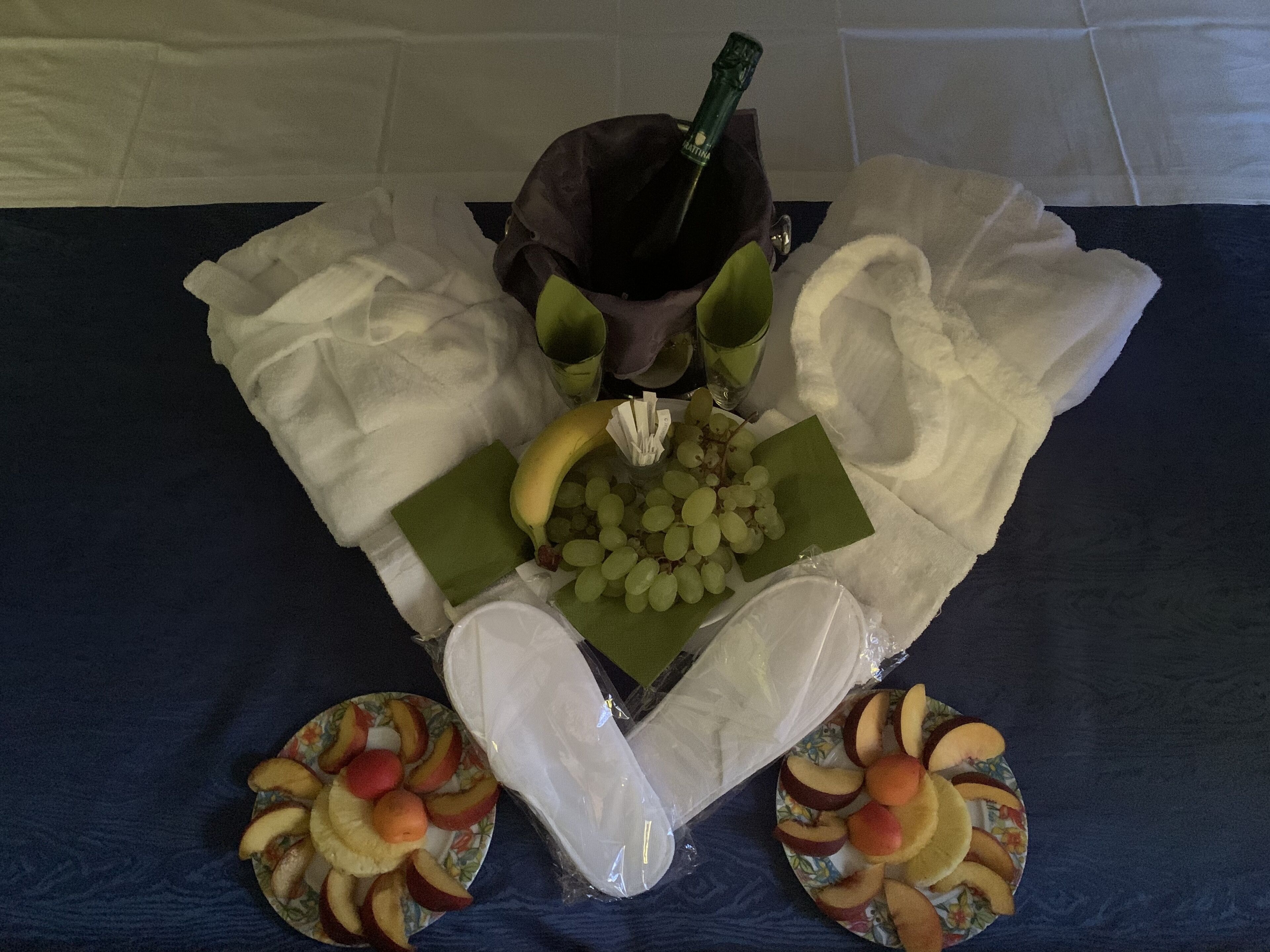 Una mesa con una botella de champán, un plátano, uvas y frutas cortadas.