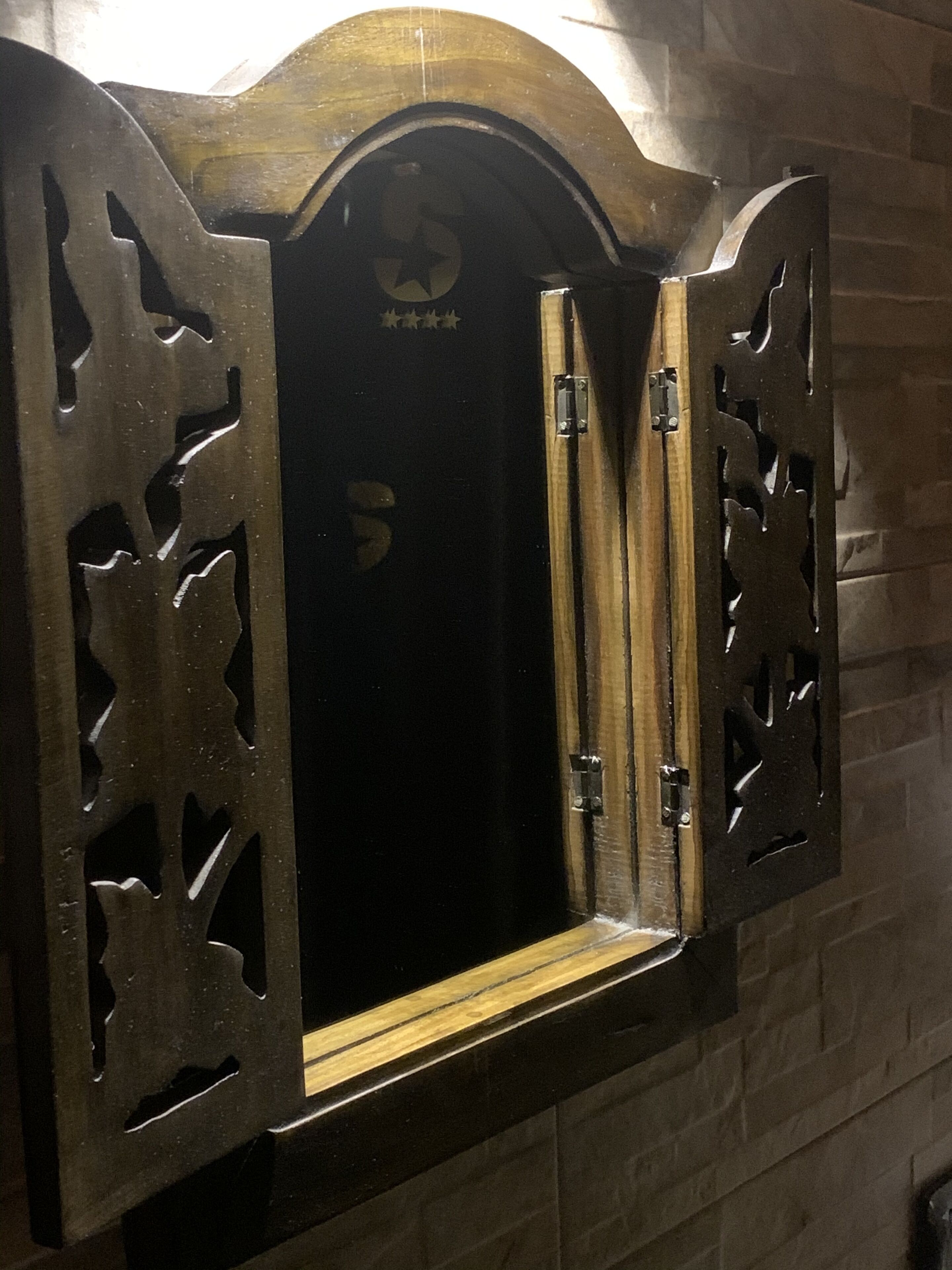 Un meuble en bois orné de motifs complexes découpés, fixé à un mur en briques.