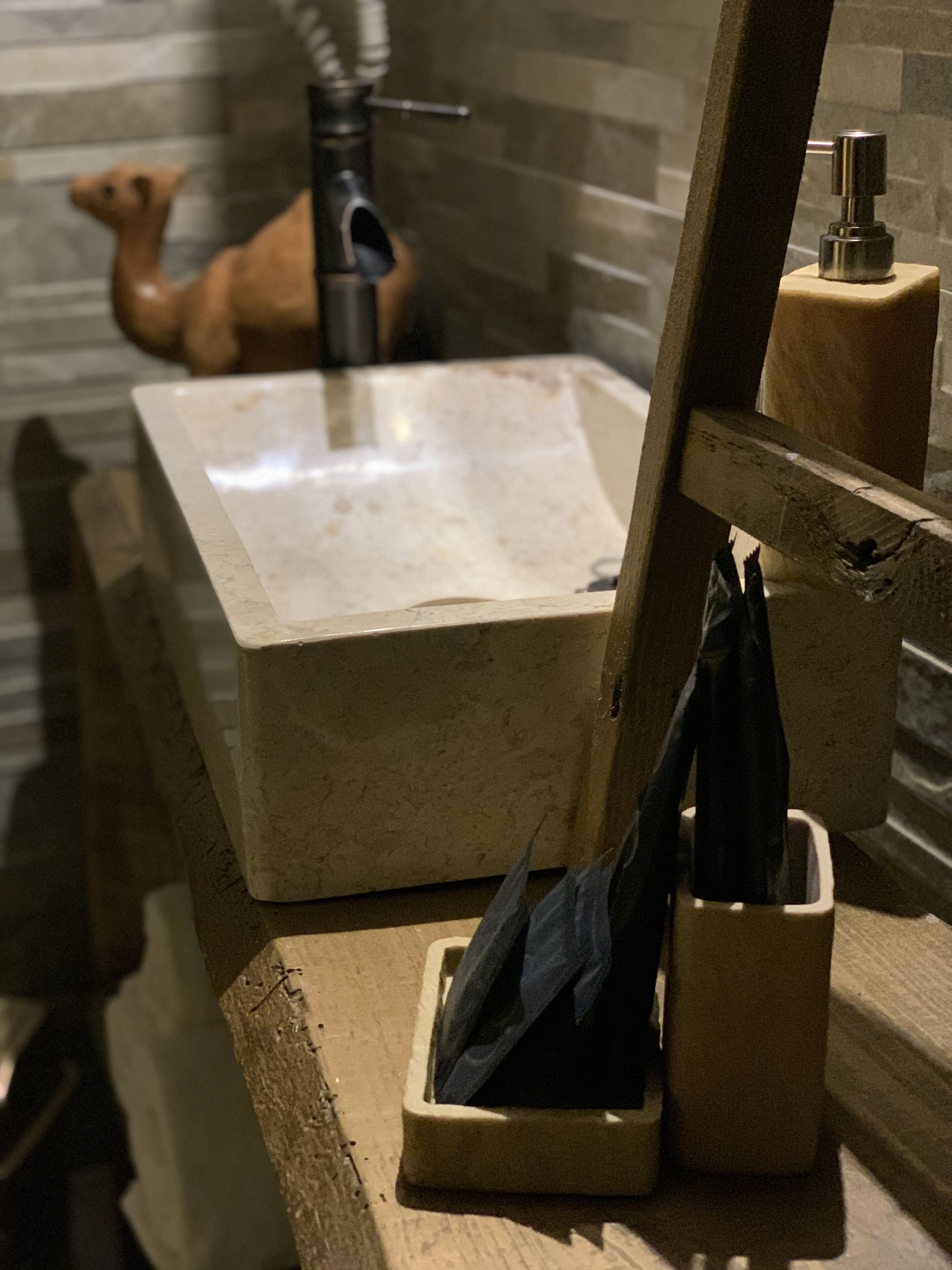 Un lavamanos con encimera de mármol, un perchero de madera y un dispensador de jabón.