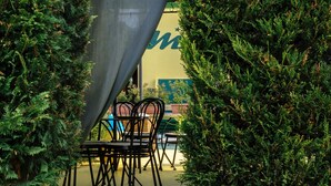 An outdoor seating area with a table and chairs, surrounded by greenery and a partially visible building. - Hotel Residence S (Front)
