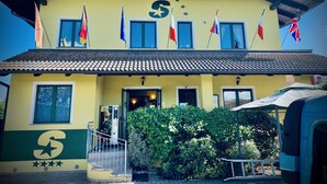 A building with a yellow facade, multiple windows, and flags. - Hotel Residence S (Front)