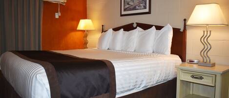 A hotel room with a bed, two bedside lamps, a nightstand, a wall-mounted air conditioner, and a framed picture.