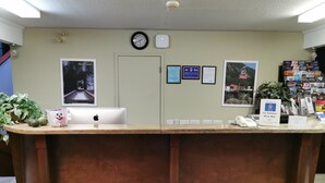 Un comptoir d’accueil avec une horloge, des certificats encadrés, un panneau d’accueil et une plante.