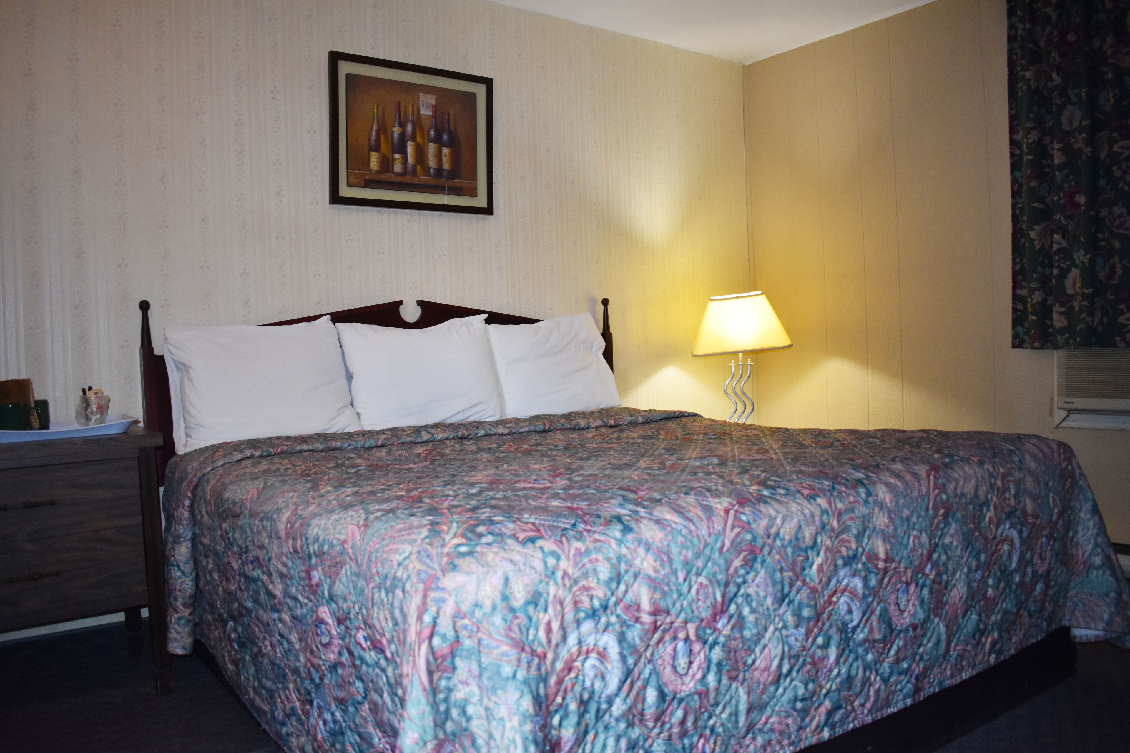A neatly made bed with a patterned bedspread, a bedside lamp, and a framed picture on the wall.