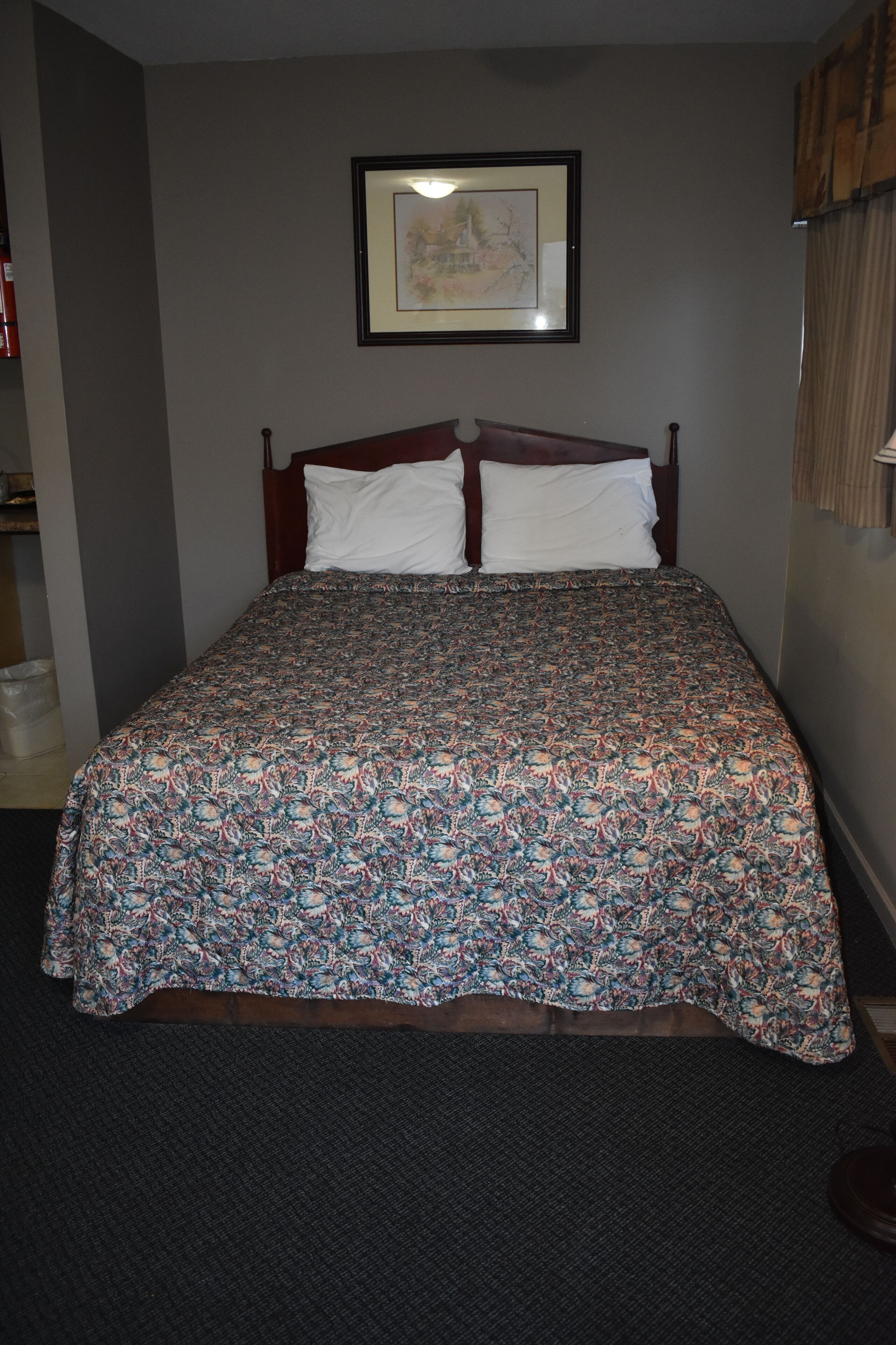 Una cama bien hecha con una colcha estampada, un cuadro en la pared y una ventana con cortinas.