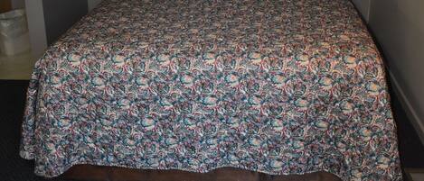 Una cama bien hecha con una colcha estampada, un cuadro en la pared y una ventana con cortinas.