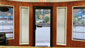 A hotel lobby with a wooden panel wall, a black door with an exit sign, and a view of the street through the door. - Hope Inn and Suites (Hope)