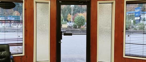 Un vestíbulo de hotel con un panel de madera, una puerta negra con señal de salida y vistas a la calle a través de la puerta.