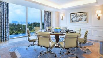A conference room with a round table, six chairs, and a city view through large windows.