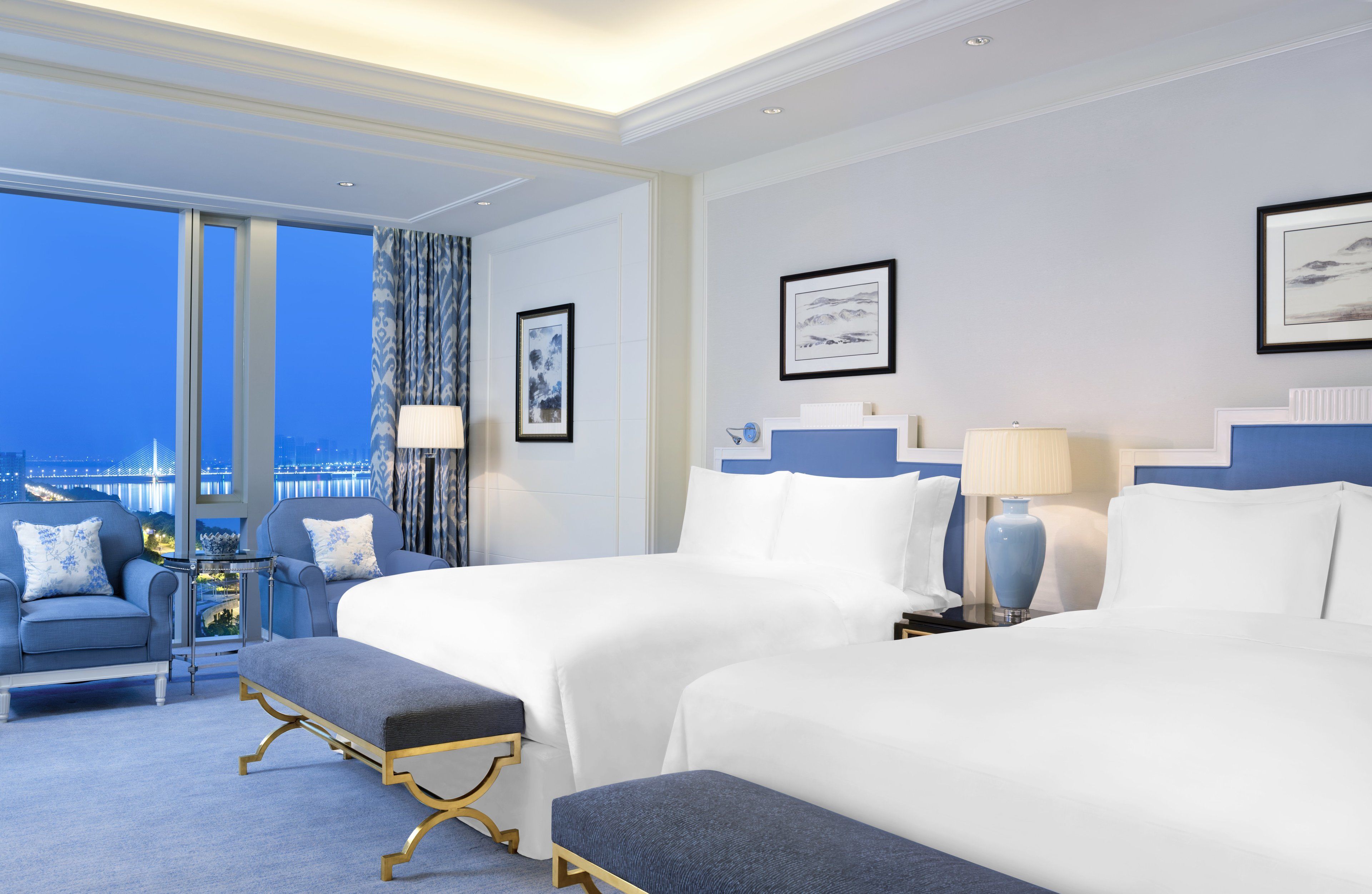 A hotel room with two beds, a sofa, a small table, and a view of a cityscape.