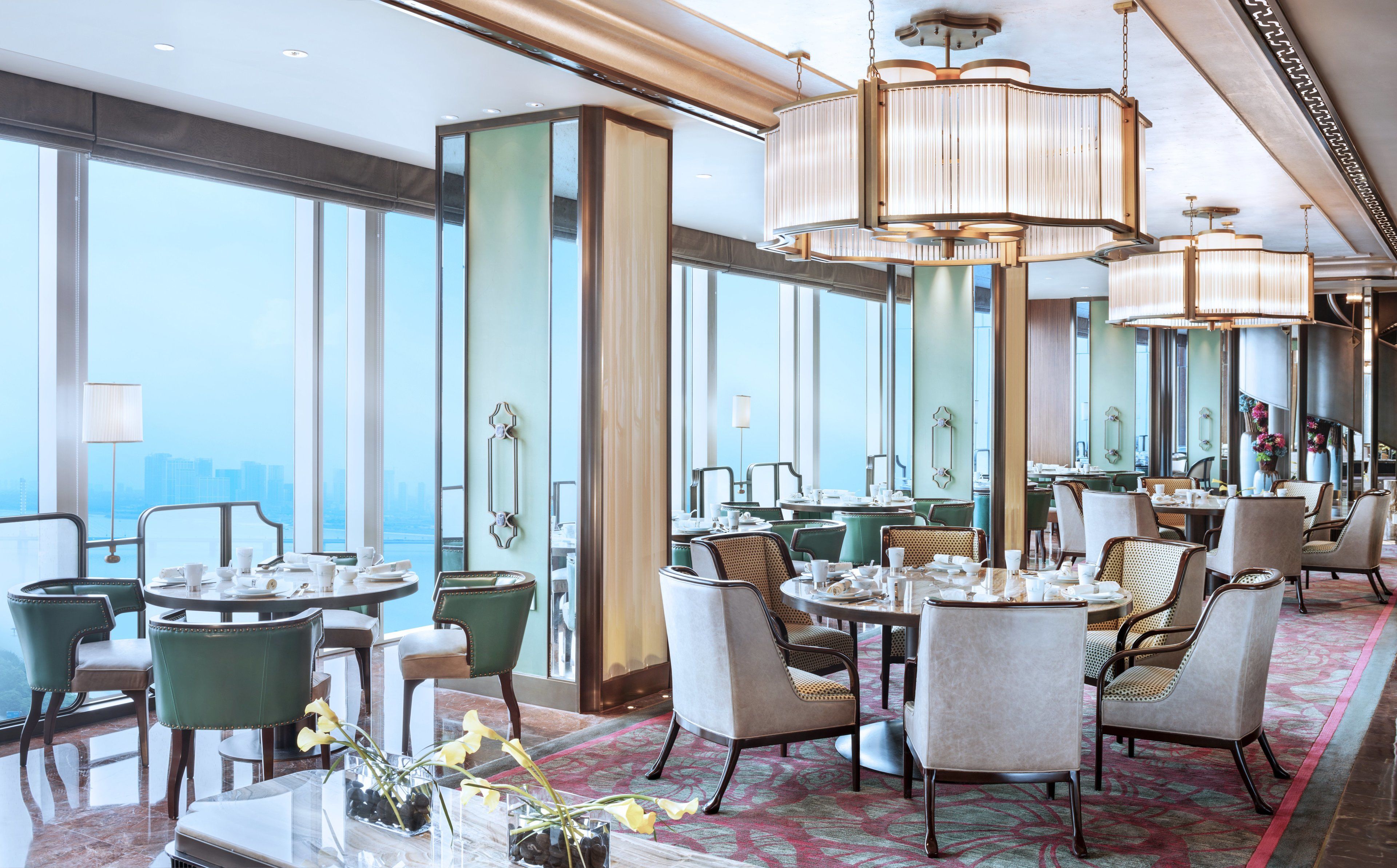 A spacious dining area with high ceilings, large windows offering a city view, and elegant chandeliers.