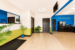 Zona de recepción de un hotel con mostrador, máquina de café y televisor instalado en la pared.