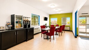 Cocina moderna con refrigerador, cafetera y zona de comedor con sillas rojas y una mesa.