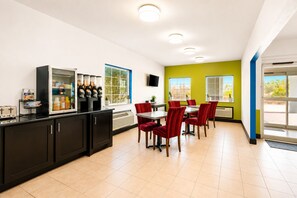 Cocina moderna con refrigerador, cafetera y zona de comedor con sillas rojas y una mesa.