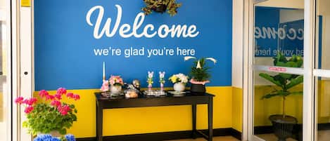A reception area with a blue wall displaying a welcome message, a black table with various items, and potted plants.
