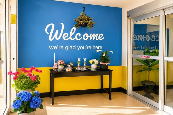 A reception area with a blue wall displaying a welcome message, a black table with various items, and potted plants.