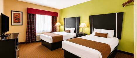 A hotel room with two beds, a desk, a television, and a window with curtains.
