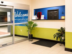 A reception area with a glass door, a welcome sign, a reception desk, a plant, and a wall with a motivational quote.