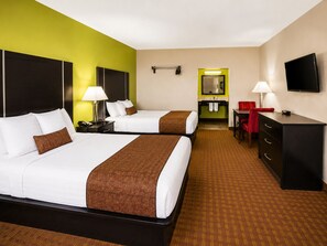 Une chambre d’hôtel avec deux lits, un bureau, une commode, une télévision et une salle de bain visible à travers une porte ouverte.