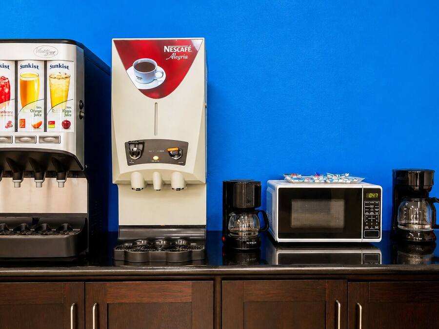 Una encimera de cocina con un dispensador de jugo Sunkist, una cafetera Nescafé, un microondas y una máquina de café.