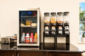 A kitchen area with a refrigerator stocked with food items and a coffee machine with multiple dispensers. - Rodeway Inn Dilley I-35 (Dilley)