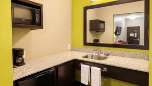 A compact bathroom with a built-in sink, a coffee maker, a microwave, and a mirror.